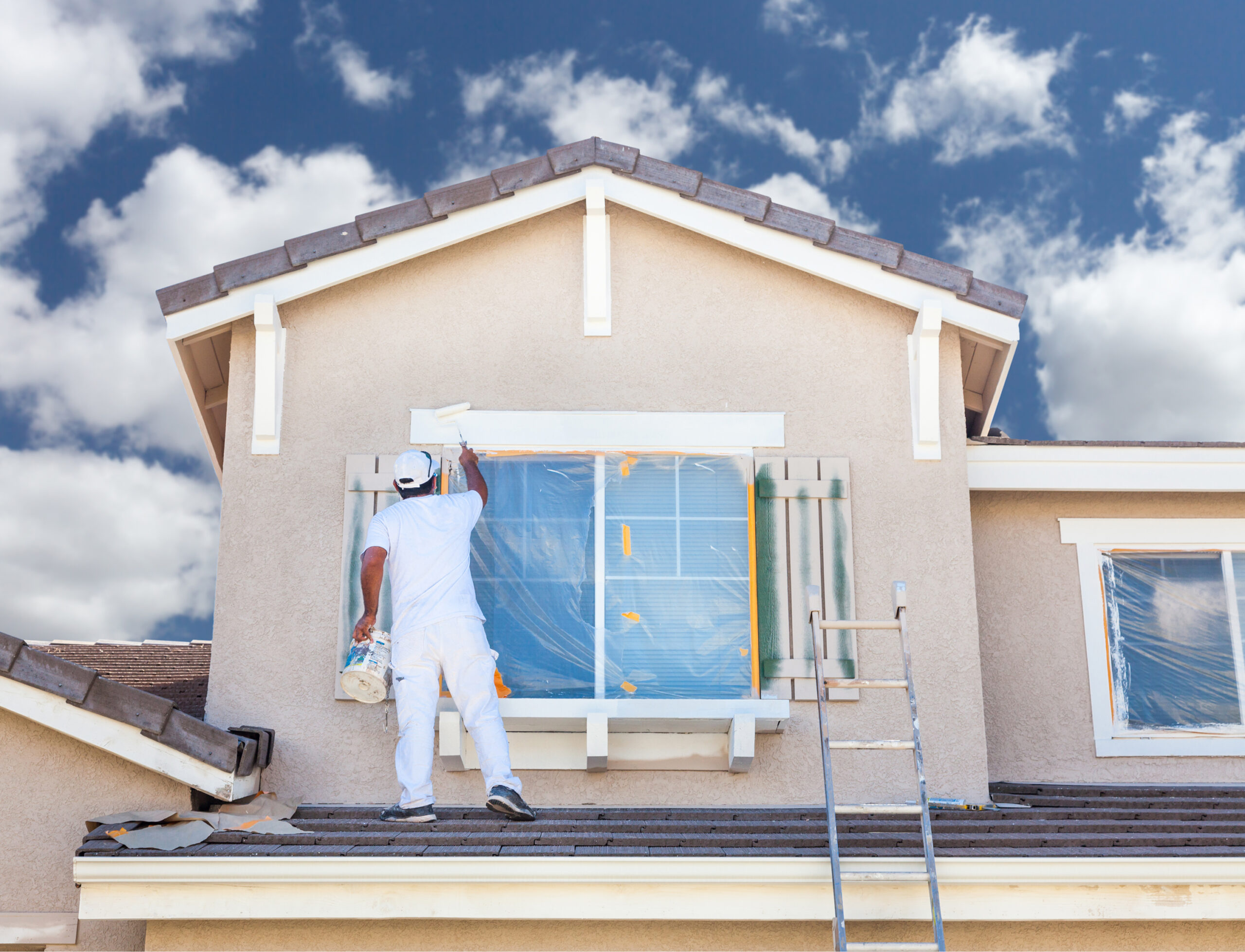a painter standing on a roof and painting window trim